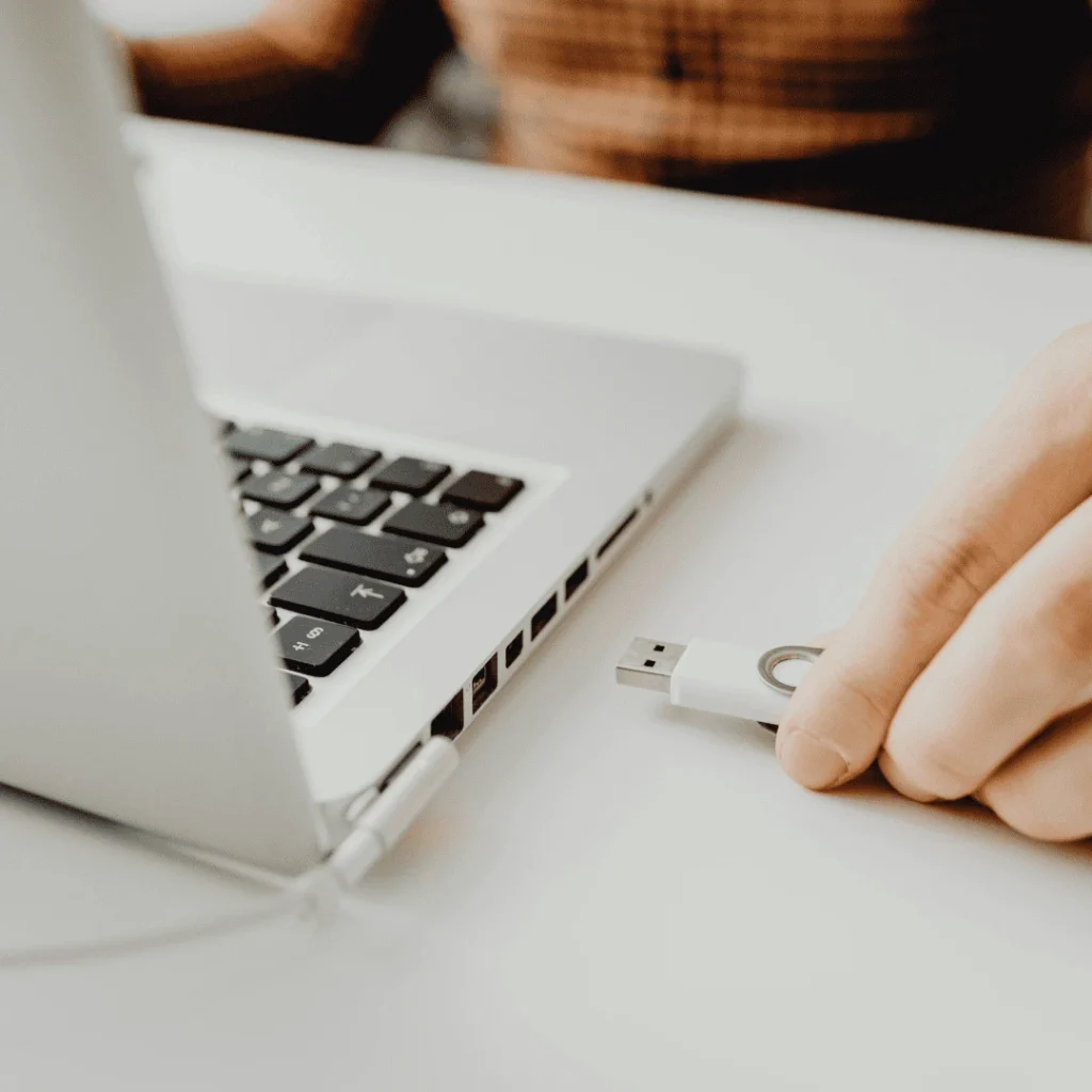 Gros plan sur une main insérant une clé USB blanche dans un ordinateur portable, illustrant l’option de récupération des photos sur clé USB avec le photobooth Ouistibox à Poitiers.